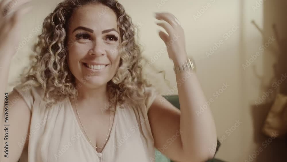 Mulher alegre sorrindo com as maos em seu lindo cabelo cacheado, sentado na cama. Cinematico 4k.