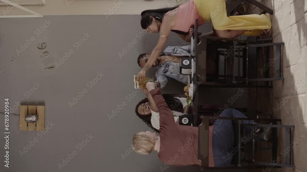 Grupo diversificado de amigos sorridentes brindando a mesa de um bar, durante o happy hour. Cinematic 4k. Video vertical.