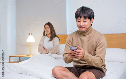 Asian husband sitting on bed in bedroom at home at night, hiding, unfaithfully cheating on his wife, using mobile phone to chat with another woman. Family, marriage issue or problem Concept. photo