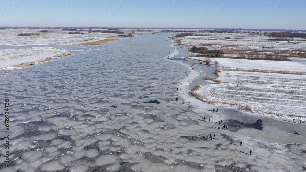 Aerial view of people near frozen river and land covered with snow on a cold winter day