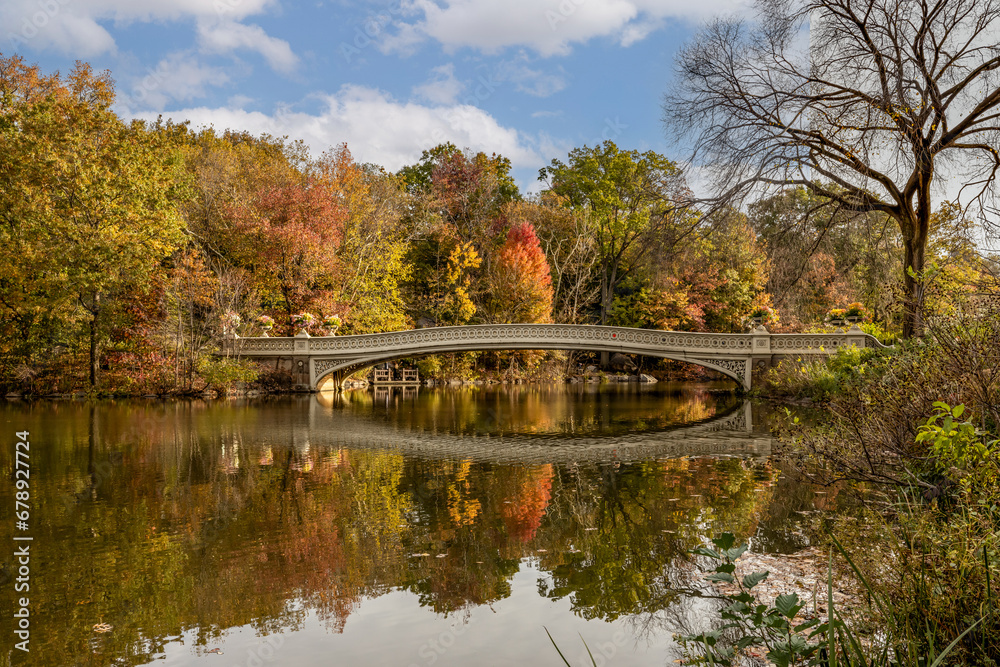 Central Park Bow Bridge autumn colors reflections in lake blue sky clouds red, orange green