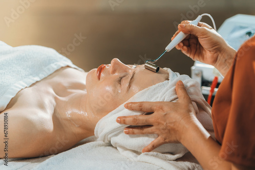 Beautiful young women lie on spa bed while having facial massage from professional doctor. Attractive female with beautiful skin surrounded by electric facial machine. Tranquility. photo