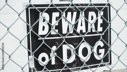 beware of dog black and white rectangle sign against diamond link silver fence with white background behind it photo