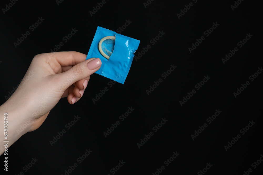 Woman holding condom on black background, closeup. Space for text Woman holding condom on black background, closeup. Space for text