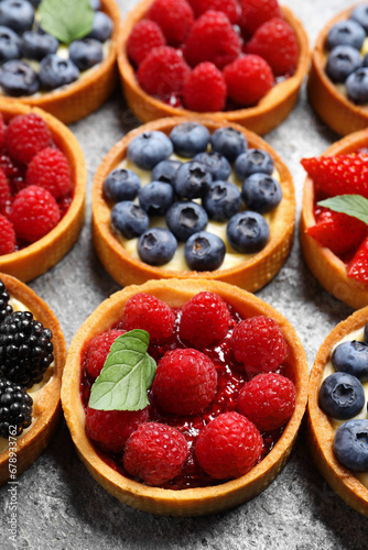 Tartlets with different fresh berries on light grey table, above view. Delicious dessert