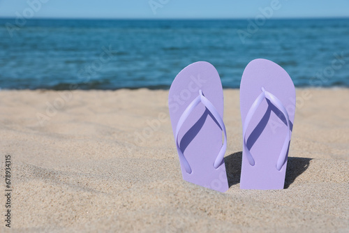 Stylish violet flip flops on beach sand, space for text