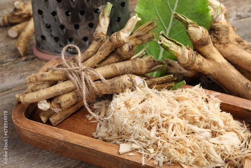 Grated horseradish and roots on wooden table, closeup photo