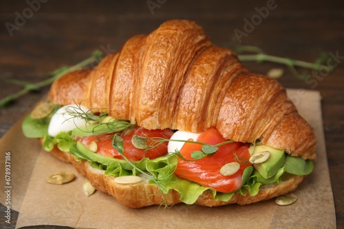 Tasty croissant with salmon, avocado, mozzarella and lettuce on wooden table, closeup