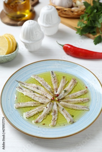 Tasty pickled anchovies with spices and products on white wooden table