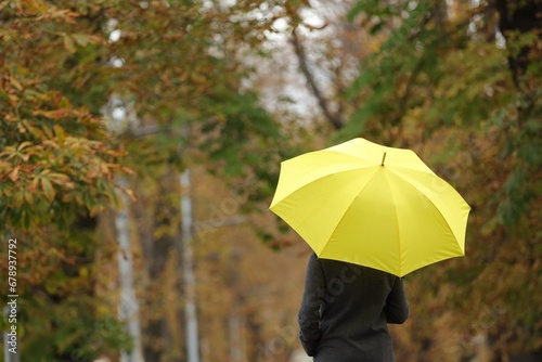 Woman with yellow umbrella in autumn park  back view. Space for text