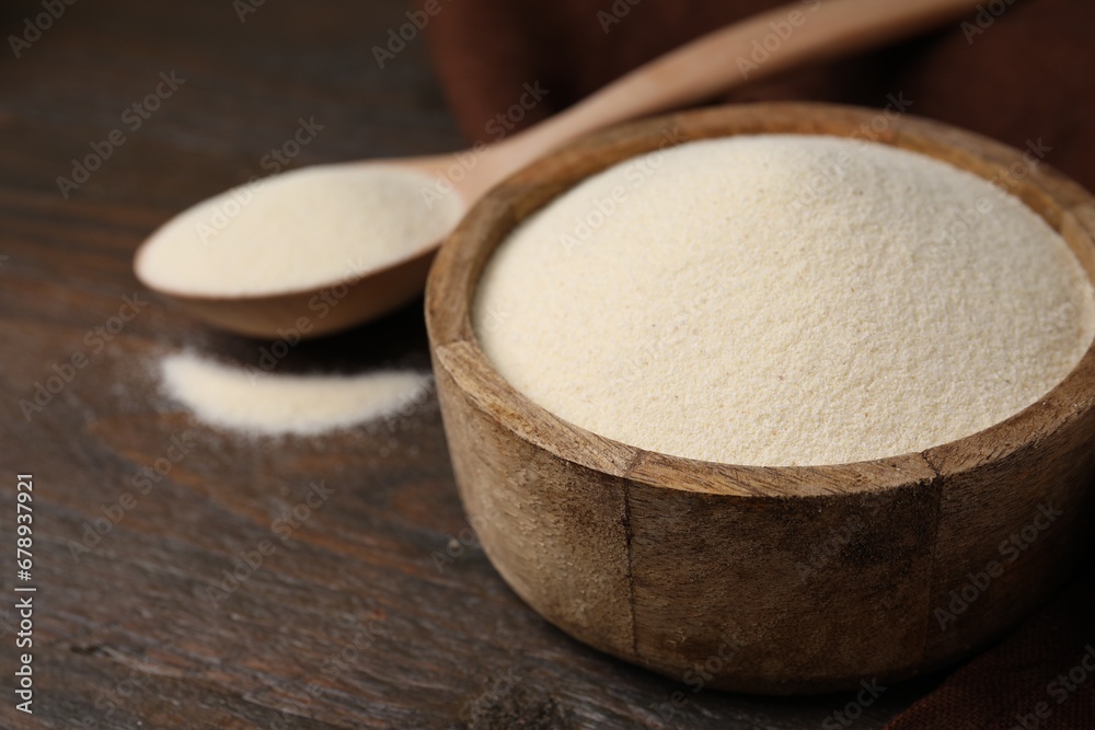 Uncooked organic semolina in bowl and spoon on wooden table, closeup. Space for text