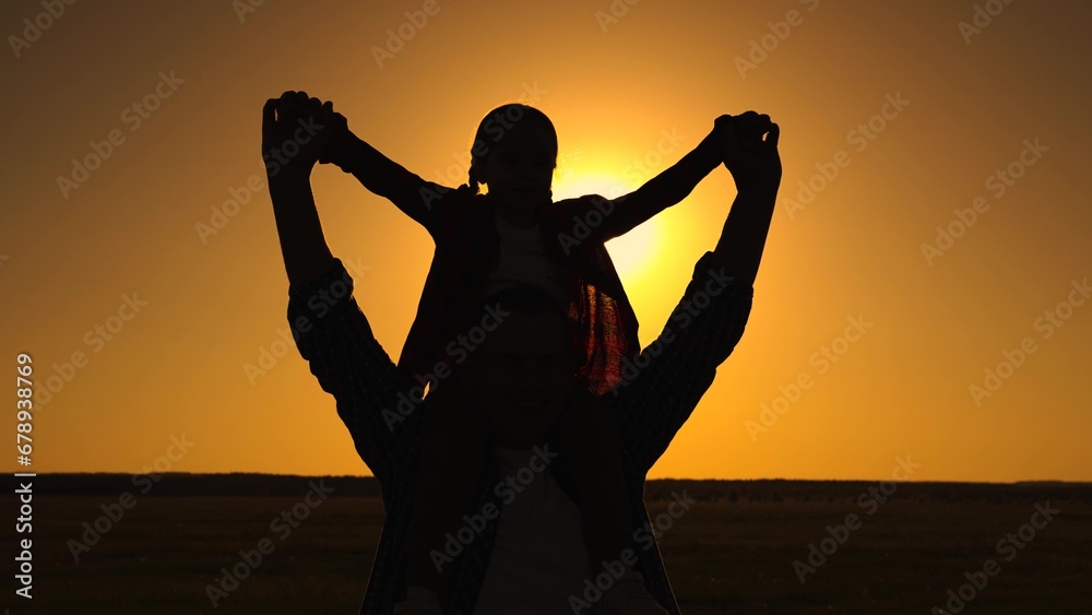 Happy family, dad, child on fathers shoulders, playing together in park against sky, mast flying, silhouette. Dad, daughter dream of flying together, family fun in outdoors. Child father walk, sunset