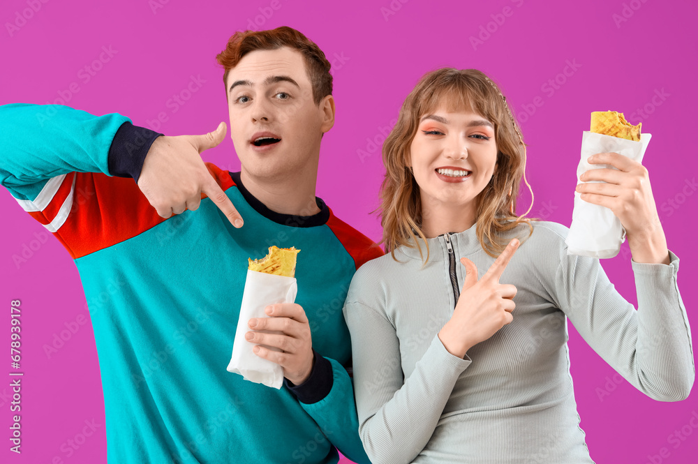 Young couple pointing at tasty sandwich wraps on purple background