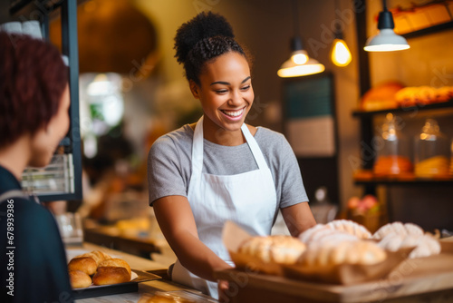 Proud and smiling African American female baker, who's also the shop owner, offering exemplary customer service as she hands a customer their order in her retail store photo