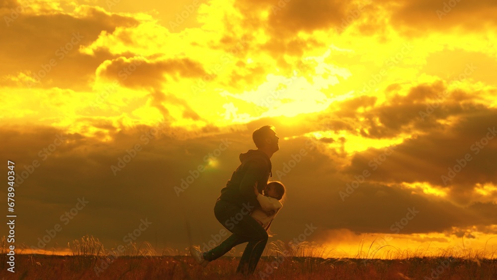 Happy dad plays with his baby daughter, throws child into sky with his hands, happy child laughs. Silhouette, father, child playing together in park against backdrop of sun clouds. Family, dream fly