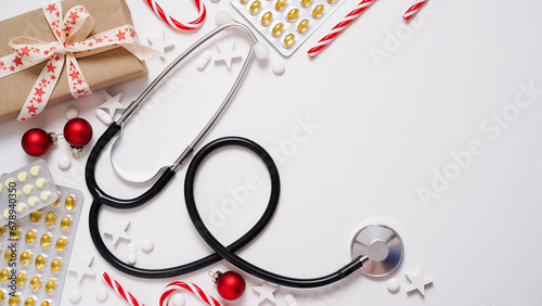 Christmas medical banner.Close-up of stethoscope,gift box,striped lollipops,red balls,stars and pills on white background,top view,flat lay,copy space.New Year's medicine, congratulations to doctor.