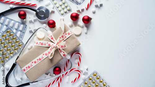 Christmas medical banner.Close-up of stethoscope,gift box,striped lollipops,red balls,stars and pills on white background,top view,flat lay,copy space.New Year's medicine, congratulations to doctor.