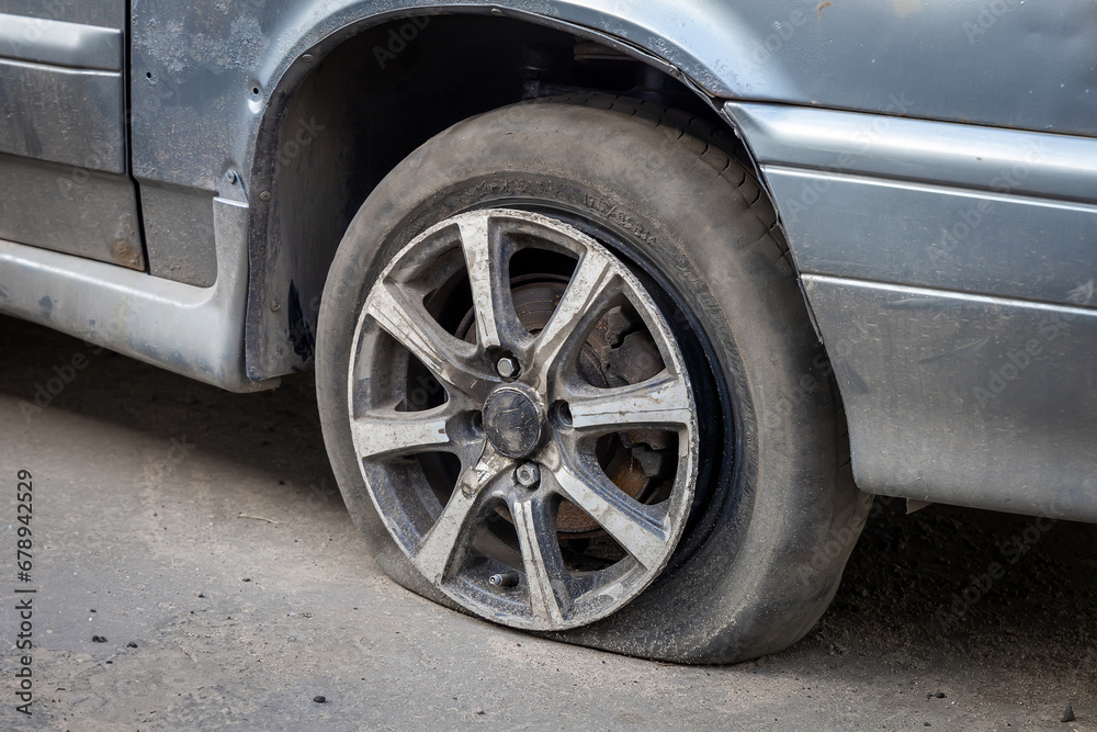 A flat tire or tear rubber tire of an old abandoned broken car on the city parking. The old rubber vehicle tire. Automobile junkyard or car dump. Scrap and recycling vehicle. Environmental problems