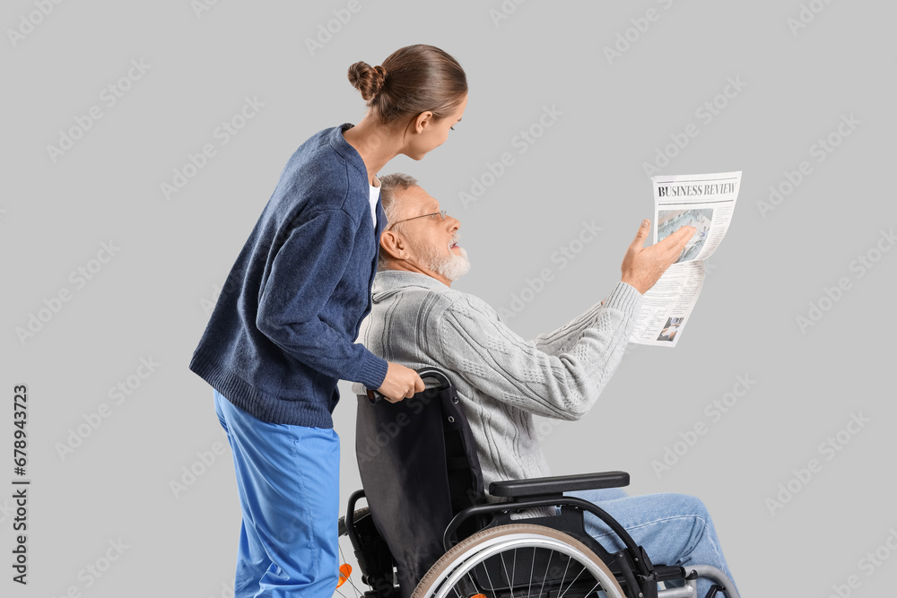 Obraz premium Senior man in wheelchair with newspaper and nurse on light background