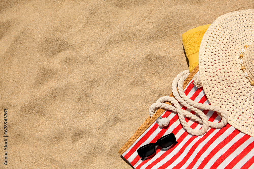 Striped beach bag, sunglasses, towel and hat on sand, flat lay. Space for text - obrazy, fototapety, plakaty 