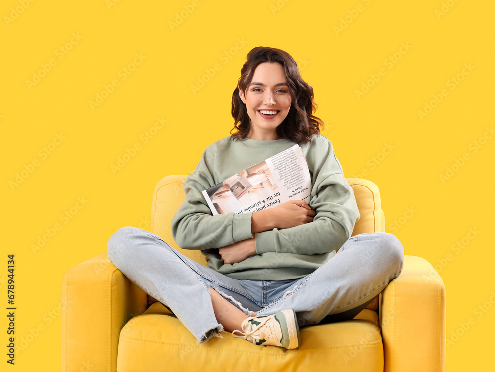 Young woman with newspaper in armchair on yellow background Young woman with newspaper in armchair on yellow background