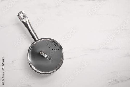 One steel saucepan with strainer lid on white marble table, top view. Space for text