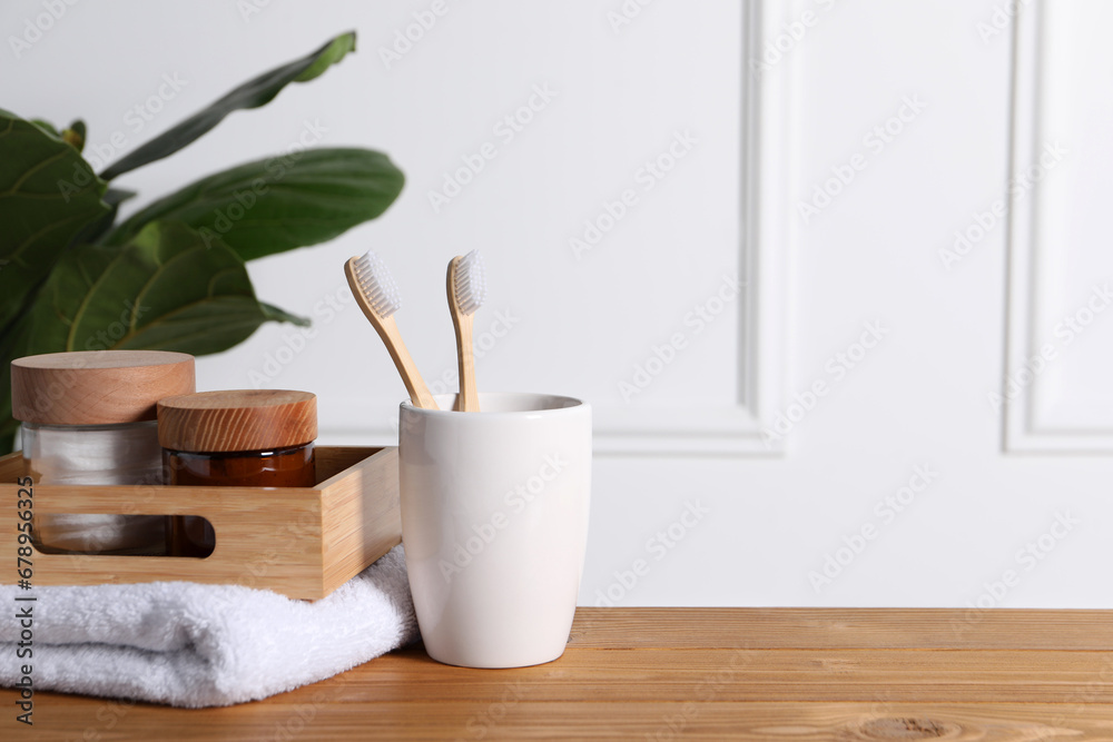 Bamboo toothbrushes in holder, towel, cosmetic products and leaves on wooden table. Space for text