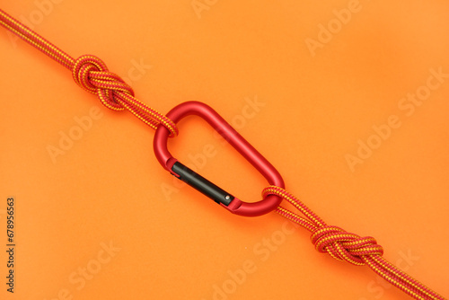 One metal carabiner with ropes on orange background, top view