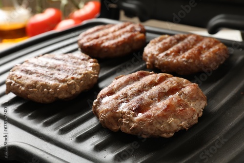 Delicious hamburger patties cooking on electric grill, closeup