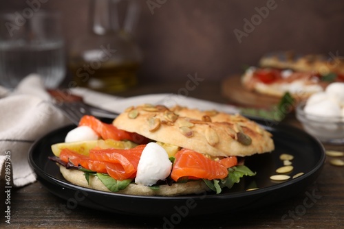 Tasty bagel with salmon, mozzarella cheese, tomatoes and lettuce on wooden table, closeup