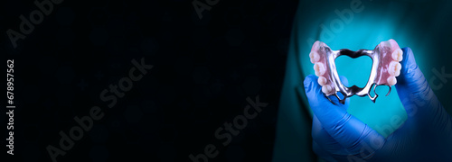 The doctor holds a cobalt chrome denture. Dentist surgeon isolated on black background shows a removable dental prosthesis.Dental clinic services concept. With space for text photo