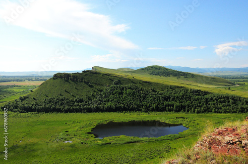 A small beautiful lake at the foot of a high hill of an unusual shape under a warm summer sky. photo