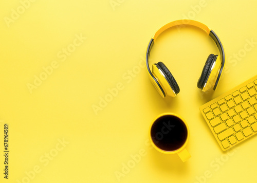 Headphones, keyboard and a cup of coffee in yellow on a yellow background.