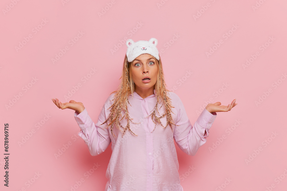 Young pregnant woman in pink home clothes and sleep mask on head stands with her arms spread to sides, morning mood concept, copy space Young pregnant woman in pink home clothes and sleep mask on head stands with her arms spread to sides, morning mood concept, copy space