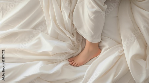 Close-up of a child's legs covered with soft white bed linen. © kept