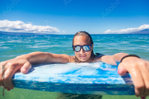 Beautiful Surfer girl floating in the ocean on her surfboard on a gorgeous sunny day. Cool reflection off her sunglasses. Horizontal photo with copy space
