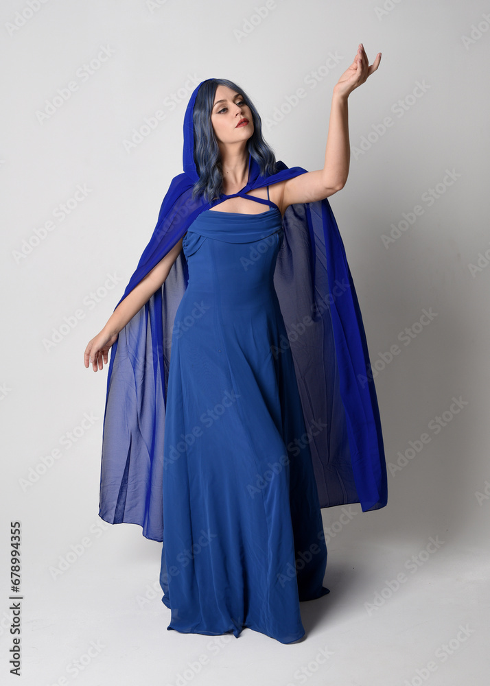 Full length portrait of beautiful female model wearing elegant fantasy blue ball gown and flowing cape with hood.
Standing pose, with gestural arms reaching out . Isolated on white studio background. Full length portrait of beautiful female model wearing elegant fantasy blue ball gown and flowing cape with hood.
Standing pose, with gestural arms reaching out . Isolated on white studio background.