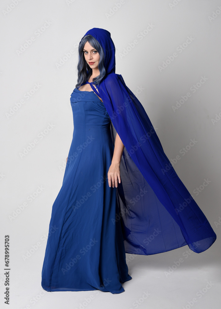 Full length portrait of beautiful female model wearing elegant fantasy blue ball gown, flowing cape with hood.
Standing pose walking away, gestural arms reaching out. Isolated on studio background Full length portrait of beautiful female model wearing elegant fantasy blue ball gown, flowing cape with hood.
Standing pose walking away, gestural arms reaching out. Isolated on studio background