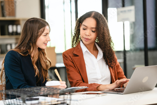 Two professional caucasian with african american businesswoman friends collaboration, working together at office, using laptop, Generally accepted audit standards, Earnings before interest and taxes photo