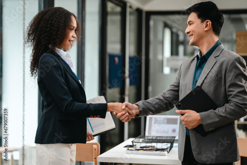 Confident Asian businessman and African American businesswoman reviewing and discussing UX/UI design elements together at desk. in formal suit