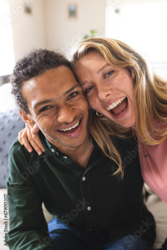 Happy diverse couple having video call and laughing in sunny living room