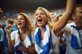 A female sports fan is happy with a group of friends, many cheering together happily and excited to watch their favorite football team. Cheering sports fans wear blue and white cheer team shirts.