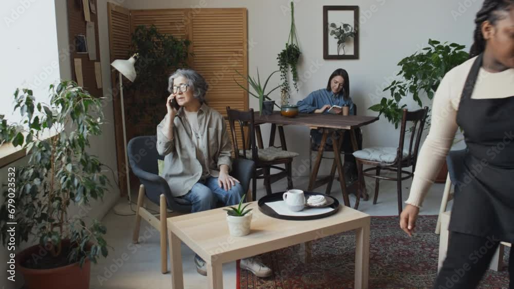 Full shot of young waitress working in coffee shop bringing to elderly female customer her order on platter Full shot of young waitress working in coffee shop bringing to elderly female customer her order on platter