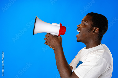 Positive african guy shouting with megaphone over blue background