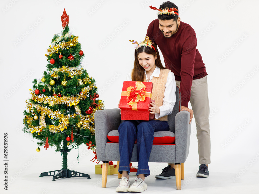 Indian bearded male boyfriend wearing reindeer antlers headband surprising Asian excited female girlfriend with present gift box celebrating New Year Christmas Eve near Xmas tree on white background Indian bearded male boyfriend wearing reindeer antlers headband surprising Asian excited female girlfriend with present gift box celebrating New Year Christmas Eve near Xmas tree on white background