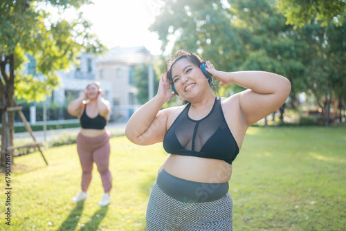 Fototapeta Naklejka Na Ścianę i Meble -  Asian plus size  woman wearing headphone while exercising in the garden at morning time. Healthy Concept.