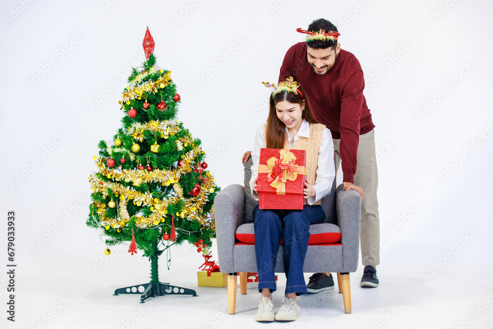 Indian bearded male boyfriend wearing reindeer antlers headband surprising Asian excited female girlfriend with present gift box celebrating New Year Christmas Eve near Xmas tree on white background Indian bearded male boyfriend wearing reindeer antlers headband surprising Asian excited female girlfriend with present gift box celebrating New Year Christmas Eve near Xmas tree on white background