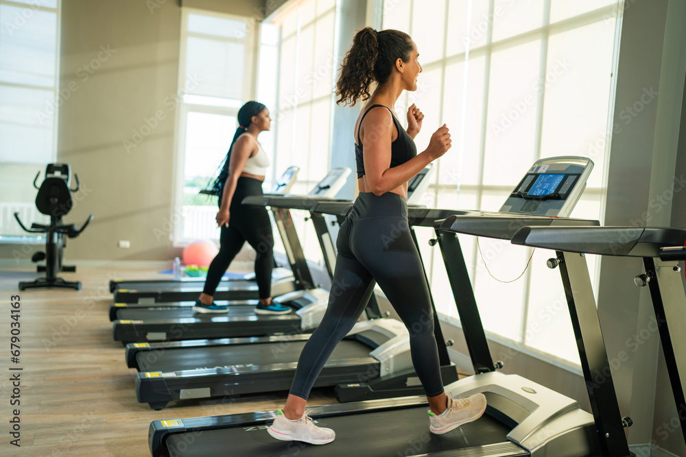Fitness exercising in gym. Sporty woman in a sports bra doing exercise by running on treadmill during a workout at the gym fitness center with group of people.