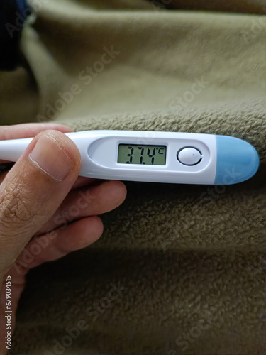 Hand holding digital thermometer on blue background