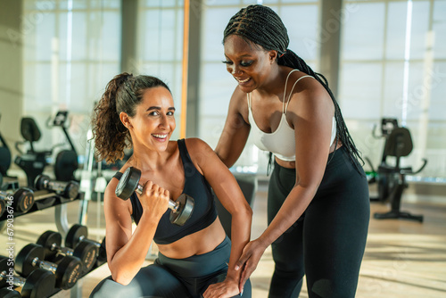 Fitness girl lifting exercising with trainer on multistation at gym for arm and shoulders muscles. Fitness exercising in gym.